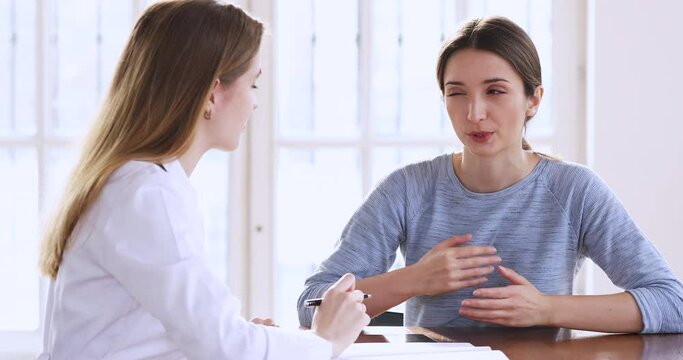 Focused young woman patient listening to female medical worker at hospital meeting. Professional physician therapist consulting millennial teen about healthcare medical insurance at clinic checkup.