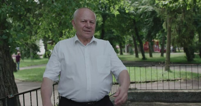 Senior man in shirt crossing hands and looking emotionally at camera outdoor