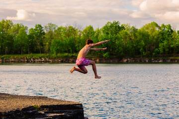 Teenage Boy Jumping off a Rock Ledge into a Lake
