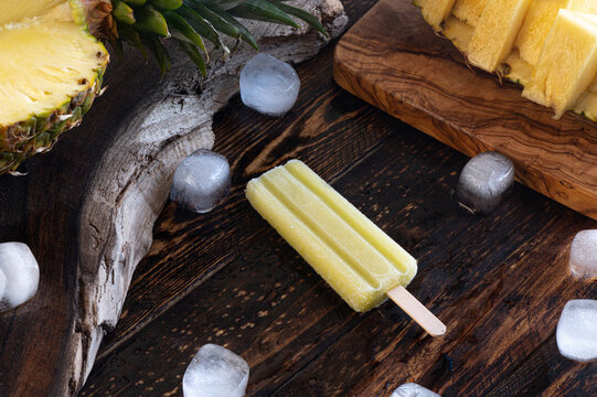 Slices pineapple, ice lollies and ice cubes over a wooden board