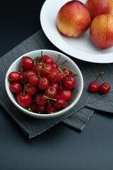A bowl of fresh cherries and a plate of peaches on a black background
