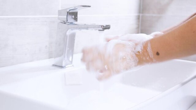 Hands of woman wash their hands in a sink with foam to wash the skin