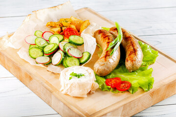 Sausages fried with sause and vegetables on wooden plate.
