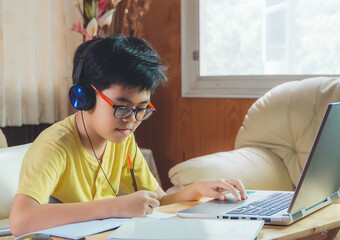 The boy wearing headphones sitting at the table with internet chat skype teacher prepare for exam...