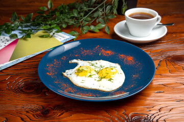 Fried eggs on a plate, black coffee. Breakfast is on the table.
