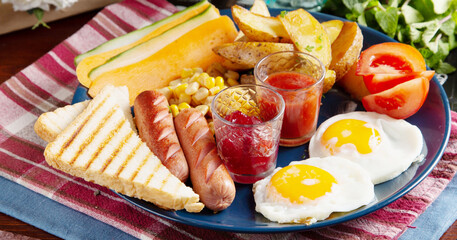 Fried eggs with grilled sausages and red sauce, grilled bread, fried potatoes. Breakfast is on the table.
