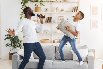 Cheerful black dad and preteen son having fun together in living room