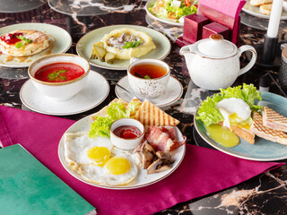 A set of several dishes for lunch, red soup borsch, sandwich, fried eggs, bacon, black tea, lunch in a restaurant or cafe
