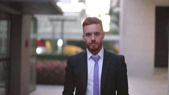 Business man walking towards camera. Handsome redhair person wearing suit in corporate center