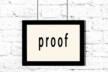 Black frame hanging on white brick wall with inscription proof - obrazy, fototapety, plakaty