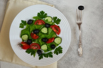 Vegetables salad with slices cherry tomato cucumber black olives with parsley and lettuce top view. The concept of healthy food and dieting. 
