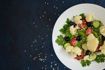 Super food fresh vegetable salad cauliflower cherry tomato cucumber sesame seed black olives with parsley and lettuce close up top view. The concept of healthy food and dieting