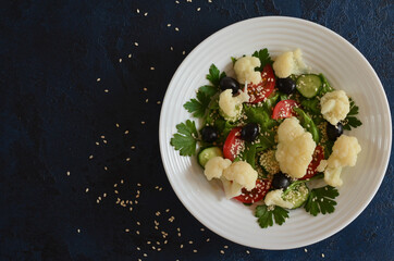 Super food fresh vegetable salad cauliflower cherry tomato cucumber sesame seed black olives with parsley and lettuce close up top view. The concept of healthy food and dieting
