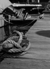 Boat lines and ropes tied to a cleat on a dock in black and white.