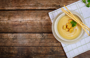 Cauliflower creamy chicken soup in gray bowl garnished with crispy croutons and italian bread sticks.