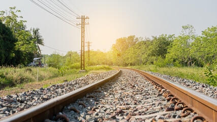 Fototapeta na wymiar The train tracks in the countryside with the sunset, orange light and light poles beside