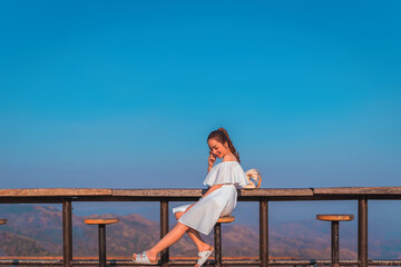 beautiful girl in white dress in holiday with sit on the chair wood in nature outdoor in sunset time by smile relaxing in vacation trip with blur background mountain at khao kho Thailand