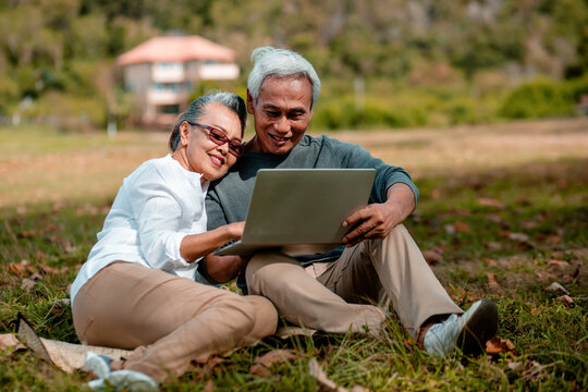 Romantic senior couple. sitting in the on green grass of the field and working on laptop. Relax and work. image not focus..Retirement age concept and love, copy space for text