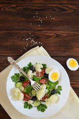 Super food fresh vegetable salad cauliflower cherry tomato cucumber sesame seed black olives with parsley and lettuce close up top view. The concept of healthy food and dieting. Copy space text