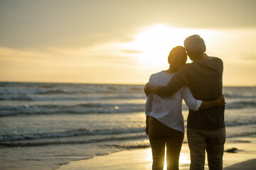 Rear view of Romantic senior embracing each other on the beach near the ocean at sunset..Retirement age concept and love, copy space for text
