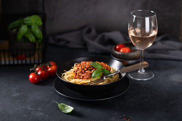 Spaghetti bolognese in a black bowl on a dark background , italian cuisine. In the background a glass of wine. Horizontal orientation