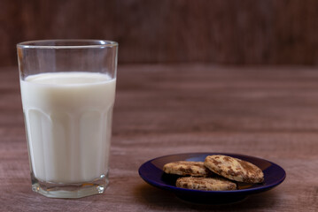 Leche en vaso de vidrio transparente con galletas de chocolate y vainilla sobre madera 