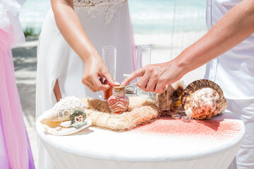 Bride and groom pouring colorful different colored sands into the crystal vase close up during symbolic nautical decor destination wedding marriage unity ceremony on sandy beach in front of the ocean 