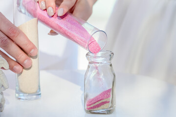 Bride and groom pouring colorful different colored sands into the crystal vase close up during symbolic nautical decor destination wedding marriage unity ceremony on sandy beach in front of the ocean 
