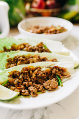 A Beautiful Display of Chicken Lettuce Wraps with a Lime Wedge with a Bowl of Ground Meat in the Background with a Bowl of Fruit.