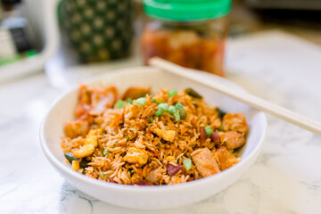 A Bowl of Korean Kimchi Fried Rice with a Pineapple and a Jar of Kimchi in the Background.