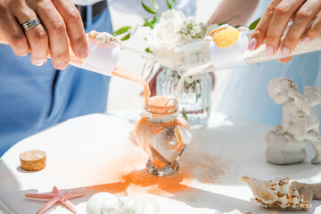 Bride and groom pouring colorful different colored sands into the crystal vase close up during symbolic nautical decor destination wedding marriage unity ceremony on sandy beach in front of the ocean 