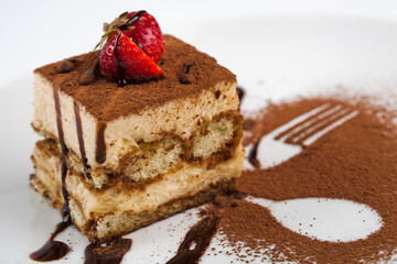 A piece of tiramisu on a white plate with a srawberry.