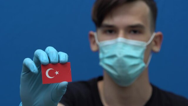 COVID-19 pandemic in Turkey. A young authentic turk man in protective medical mask and gloves holding the flag of Turkey. The Coronavirus