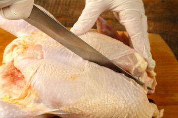 Woman cuts chicken carcass in half with a knife on a wooden board. © finist_4