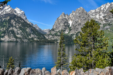 Jenny Lake Reflecting the Sky with Pine Trees and Mountains Surrounding, Behind a Rock Wall, Grand Teton National Park, Wyoming