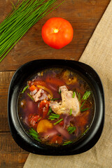 Black dish of vegetable soup on a tablecloth on a wooden table.