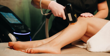 Caucasian woman lying on the couch in a spa salon and having a leg epilation session with laser...