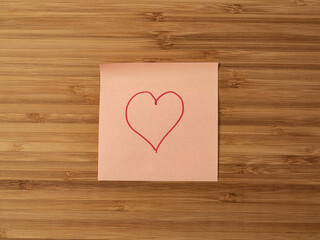 A paper sticker pasted on a wooden surface with the image of the heart symbol