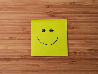 A paper sticker pasted on a wooden surface with the image of the happy smiley character