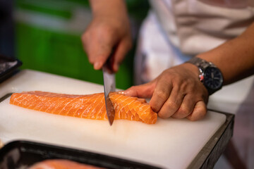 A cooking chef is cutting or slicing a piece of salmon meat for preparation a Japanese food dining in luxury restaurant. Close-up and selective focus photo.