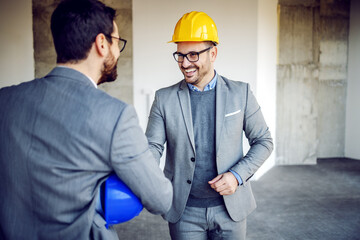 Handsome caucasian friendly real estate agent introducing himself to investor. Building in...