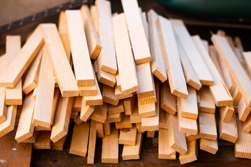 A pile of wooden even bars in the shape of a dash. Billets in a carpentry workshop, a sawmill. Pieces of wood, blanks for future crafts and furniture