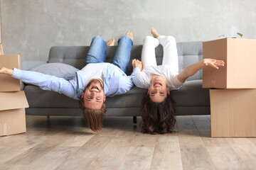 Young couple laying on the sofa with heads relaxing upside down smiling at the camera in the living...