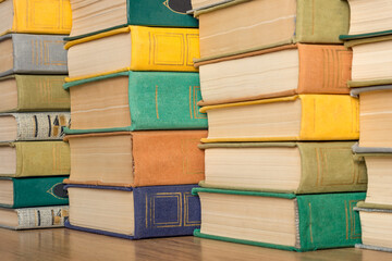 A stack of multi-colored old hardback books and textbooks on a shelf in a library.