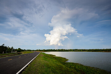 Picture of natural atmosphere along the way in the evening time, on the right is a lake, In the middle of the picture is a large white cloud.