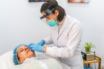 A doctor with a protective screen applying injections with security measures. Beauty salon center....