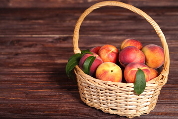 Fresh peaches with green leafs in basket on brown wooden table