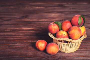 Fresh peaches with green leafs in basket on brown wooden table