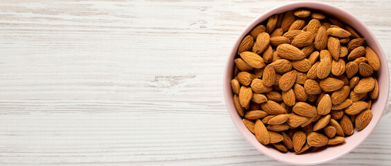 Almonds in a pink bowl on a white wooden surface, top view. Overhead, flat lay, from above. Copy space.