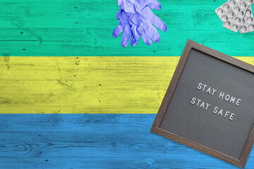 Gabon flag background on wooden table. Stay Home writing board, surgery gloves, pills with minimal...